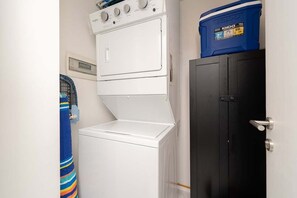 Ein Waschraum mit einer übereinander gestapelten Waschmaschine und einem Trockner, einer blauen Aufbewahrungsbox und einem schwarzen Schrank.