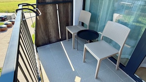 Ein Balkon mit Metallgeländer, zwei Stühlen, einem kleinen Rundtisch und Blick auf ein grünes Feld.