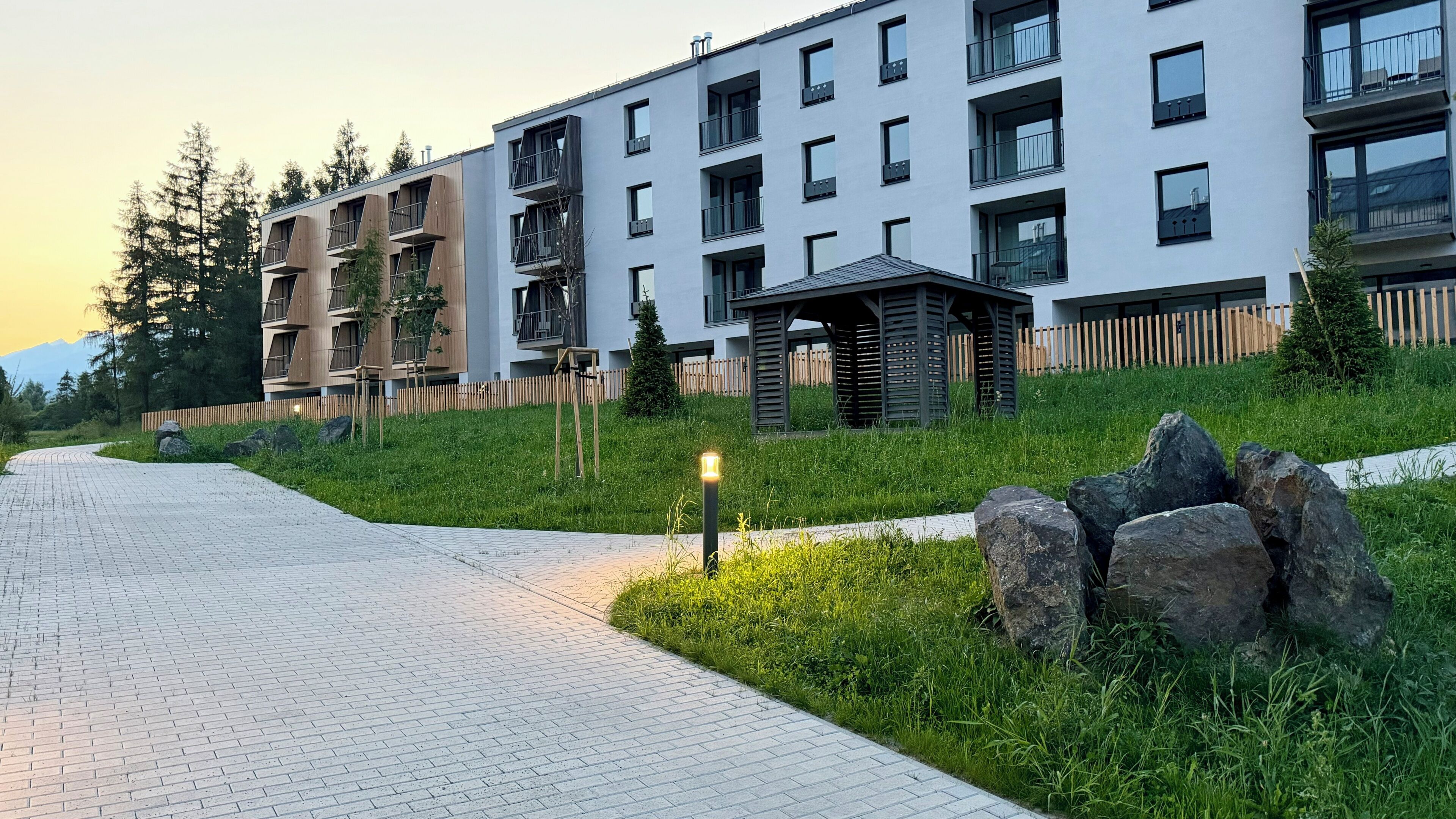 A modern residential building with multiple balconies, a paved pathway, and a small garden area.