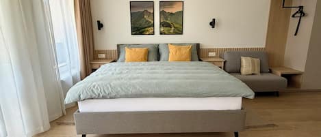 Una habitación de hotel moderna con una cama grande, un área de descanso y dos cuadros de paisajes en la pared.