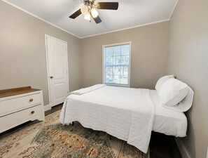 Un dormitorio con cama, cómoda, ventilador de techo y ventana con persianas.