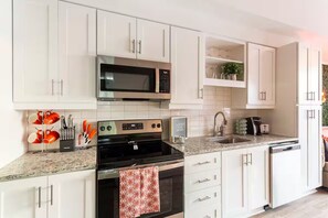 A modern kitchen with white cabinets, stainless steel appliances, and a granite countertop. - Music City Paradise - 5 min Walk to Broadway (Nashville)