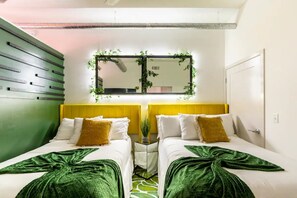 Ein Hotelzimmer mit zwei Betten, einer grünen Wand, einem Spiegel mit Pflanzen und einem gelben Kopfteil.