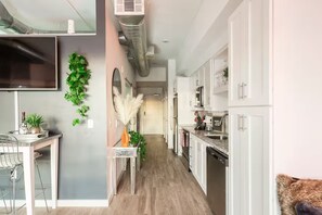 A modern kitchen with white cabinets, a dining area with a table and chairs, and a hallway with a plant. - Music City Paradise - 5 min Walk to Broadway (Nashville)