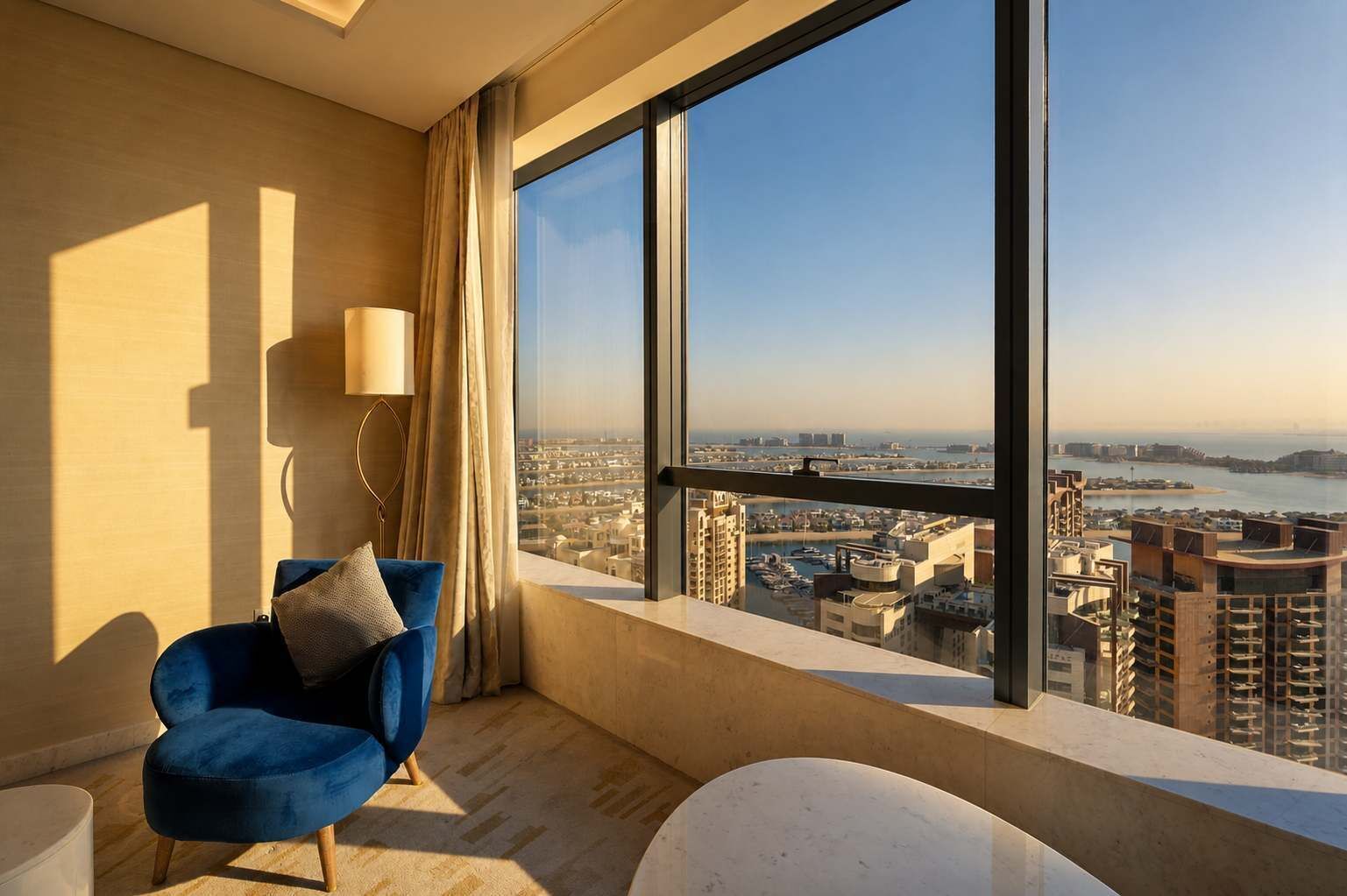 Ein modernes Zimmer mit einem großen Fenster, einem blauen Sessel, einem weißen Tisch und einer Lampe.