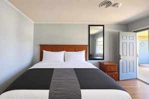 Una habitación de hotel con cama, mesita de noche, espejo y puerta.