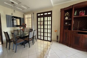 A dining area with a glass table and chairs, a wooden cabinet with decorative items, and a large window with a view.