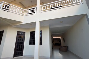 Un edificio de varios niveles con una columna central, dos puertas de marco oscuro y un corredor cubierto que conduce a un espacio interior.