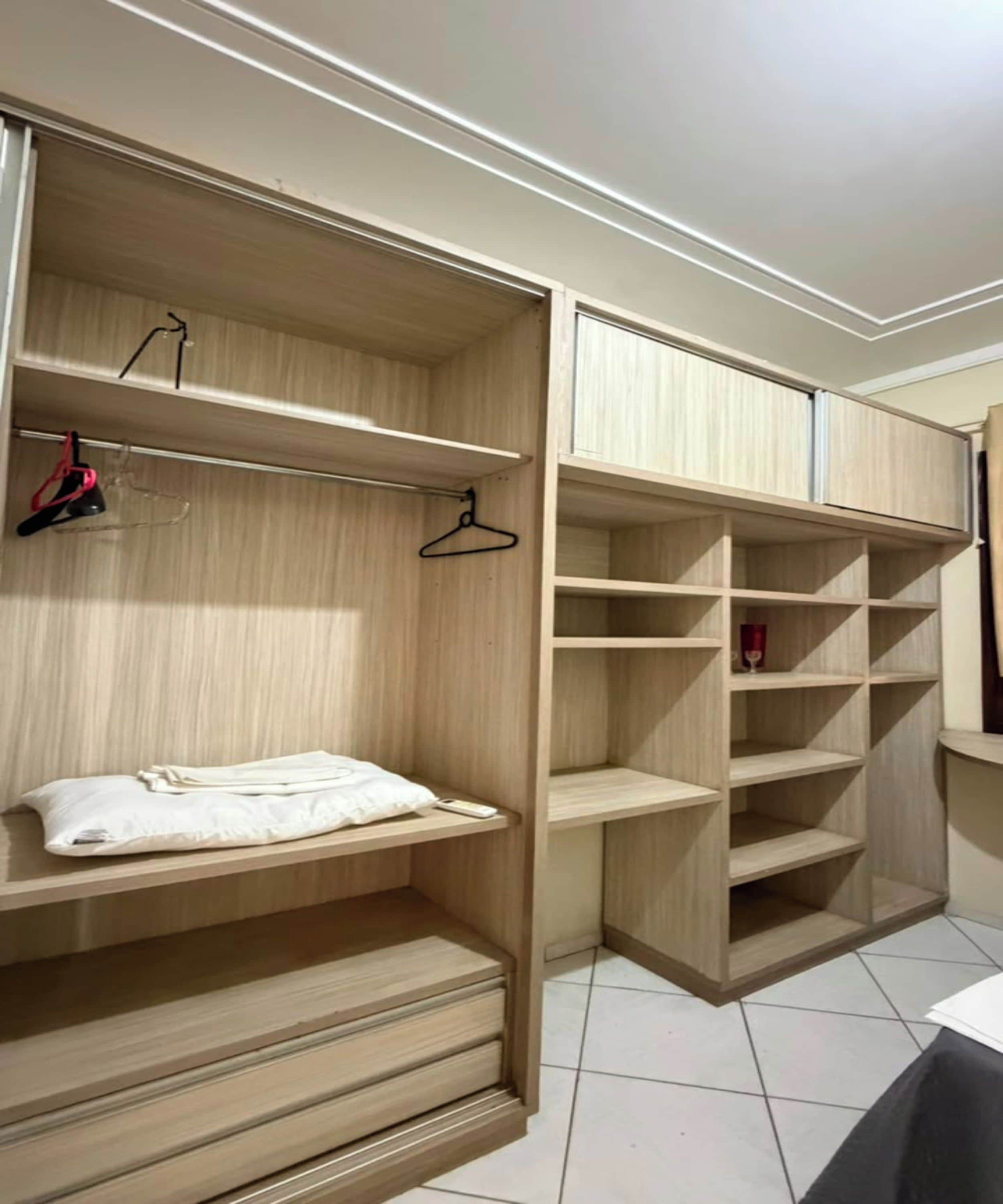 Ein begehbarer Kleiderschrank mit mehreren Regalen und Platz zum Aufhängen, ein Bett mit weißer Bettdecke und ein gefliester Boden.