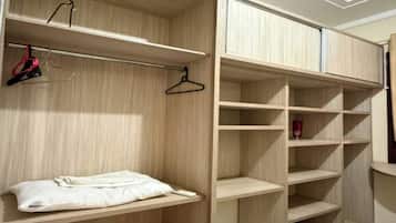 Ein begehbarer Kleiderschrank mit mehreren Regalen und Platz zum Aufhängen, ein Bett mit weißer Bettdecke und ein gefliester Boden.