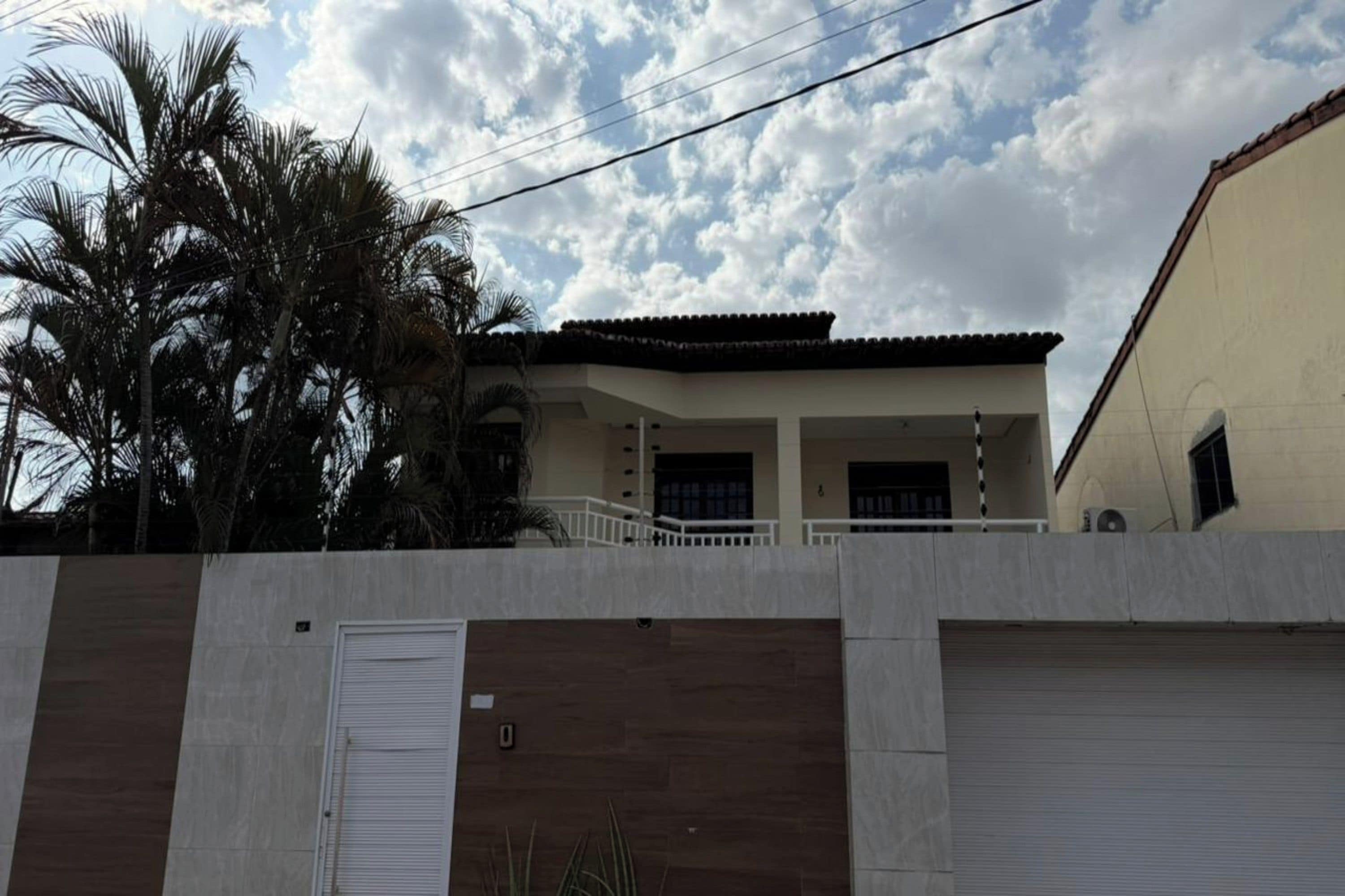 Un edificio residencial con un porche cubierto, una entrada protegida por una reja y una palmera al fondo.