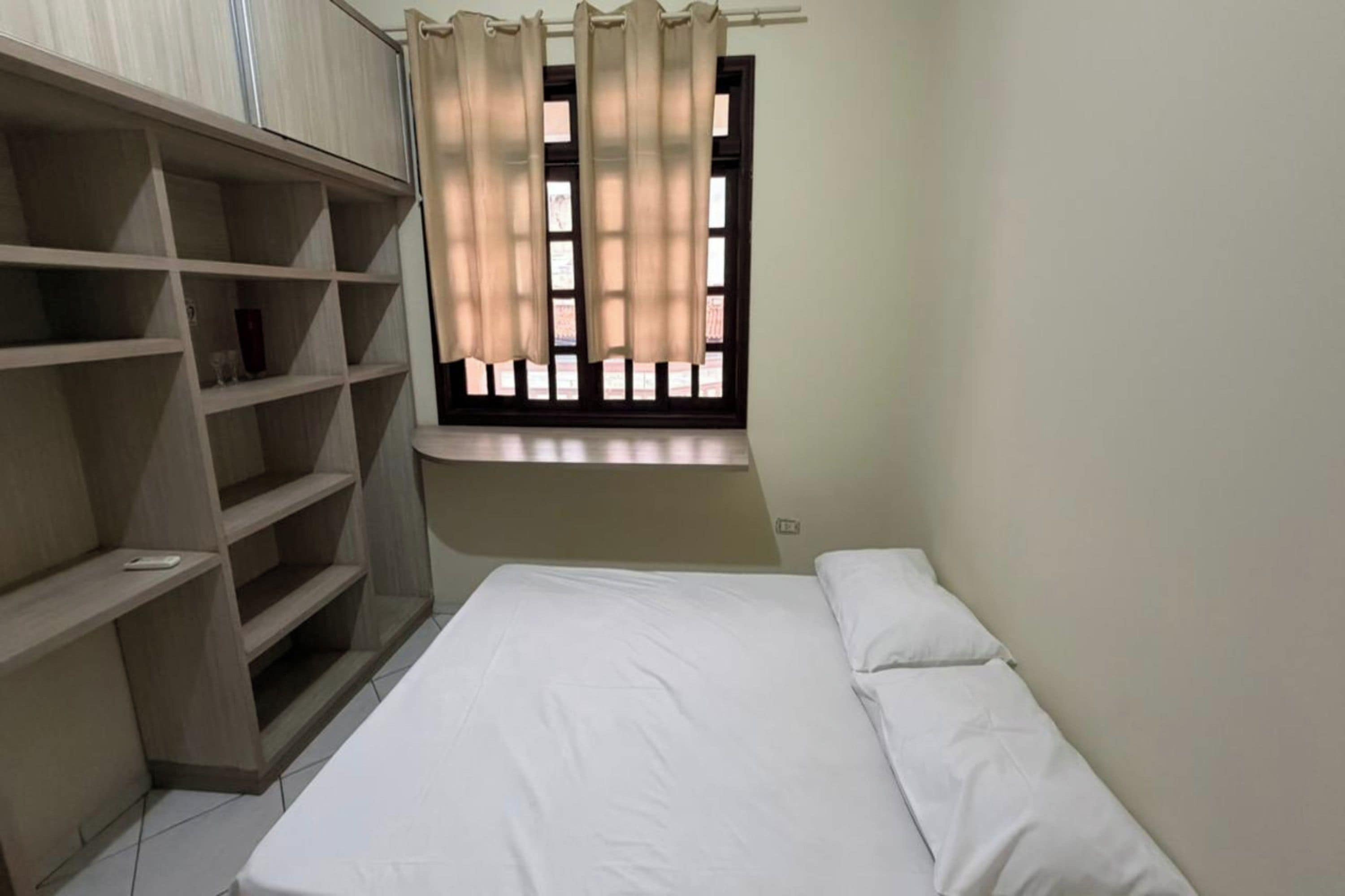 A bedroom with a bed, a window with curtains, and built-in shelving.