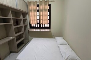 A bedroom with a bed, a window with curtains, and built-in shelving.