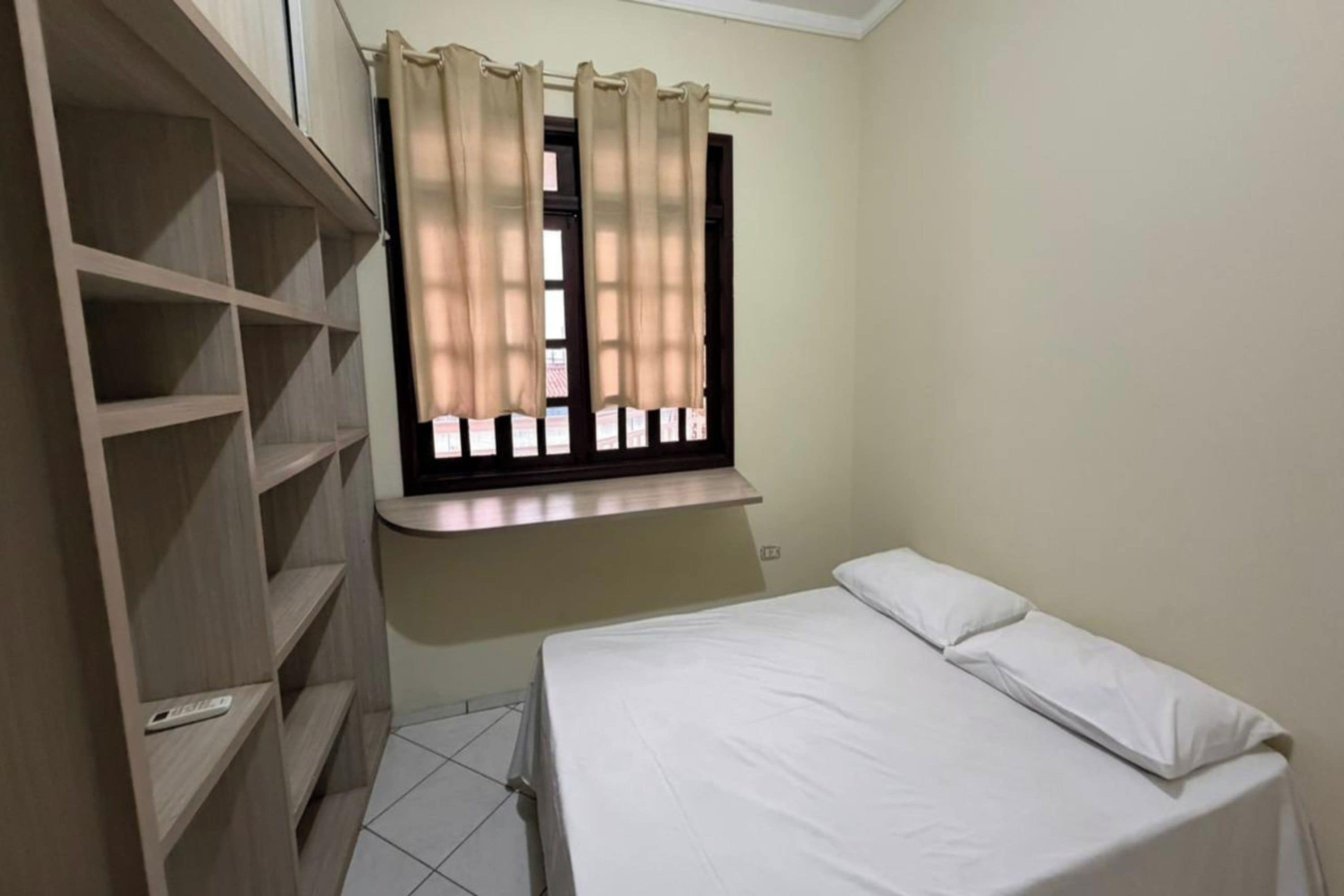 A bedroom with a bed, a window with curtains, and a wooden wardrobe.