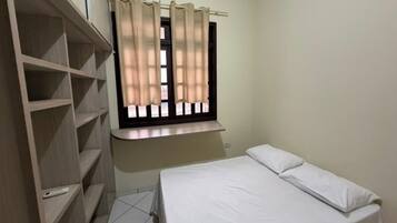 A bedroom with a bed, a window with curtains, and a wooden wardrobe.