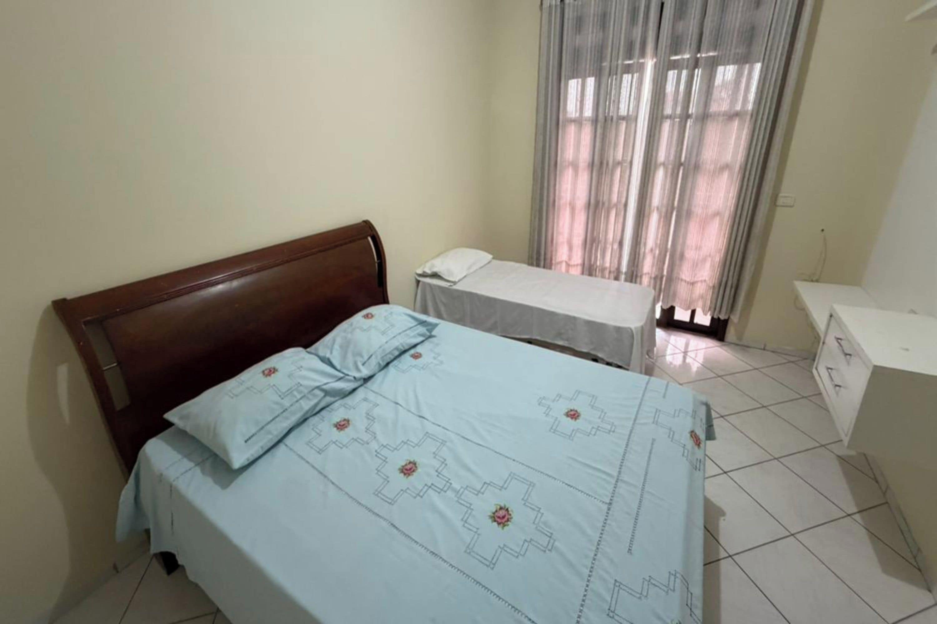 Quarto com cama, mesa de cabeceira e janela com cortinas.