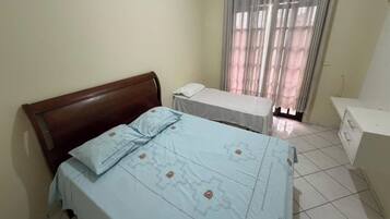 Quarto com cama, mesa de cabeceira e janela com cortinas.