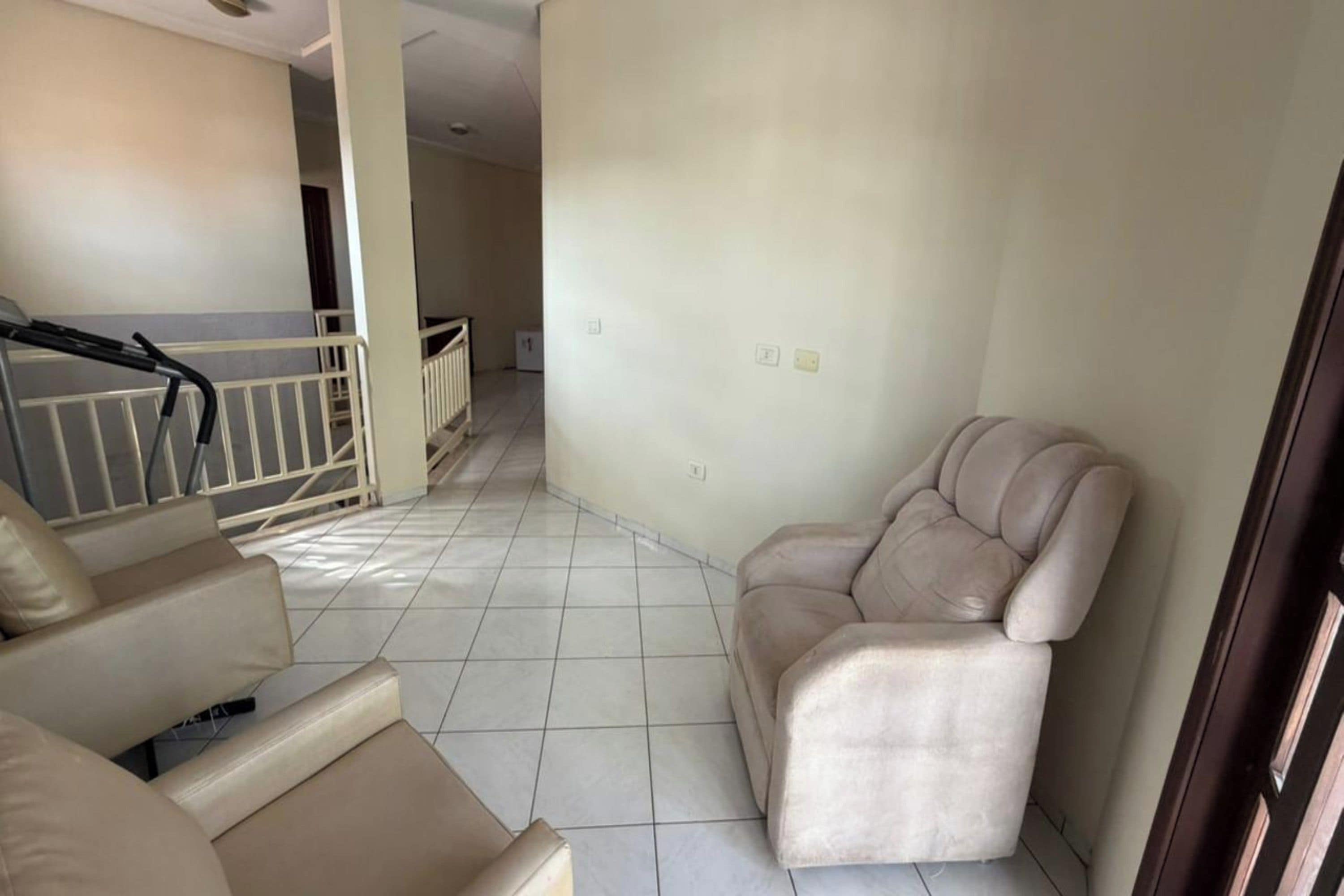 Een woonkamer met een beige bank, een stoel en een trap die naar een ander niveau leidt.