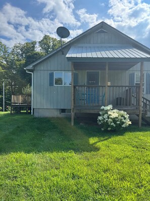 A single-story house with a porch, a satellite dish, and a small garden. - Cozy 1-bedroom house in pleasant Guilford with AC (Guilford)