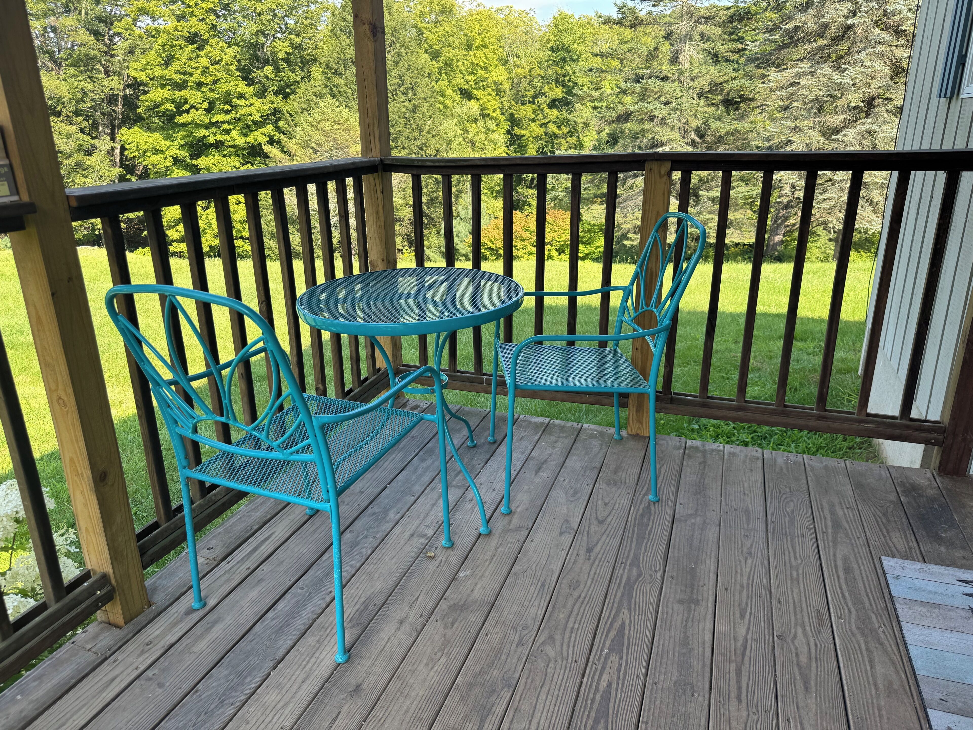 A wooden deck with two turquoise metal chairs and a small round table.