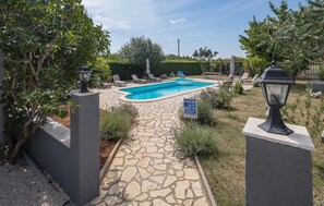 A swimming pool with a stone pathway leading to it, surrounded by greenery and outdoor furniture. - Nice home in Porec with swimming pool (Porec)