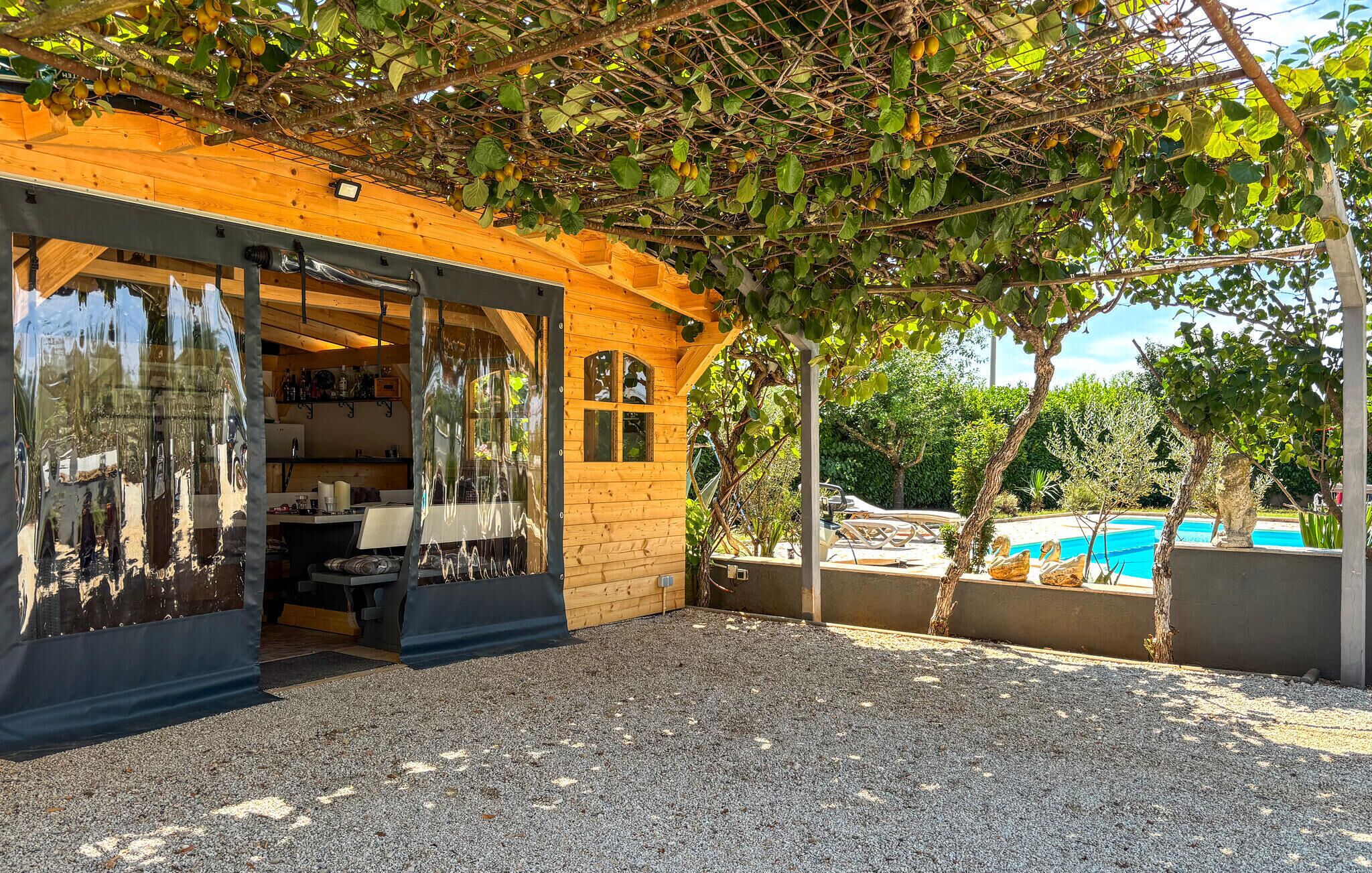 A wooden structure with a glass door, a pool, and a pergola with climbing plants.