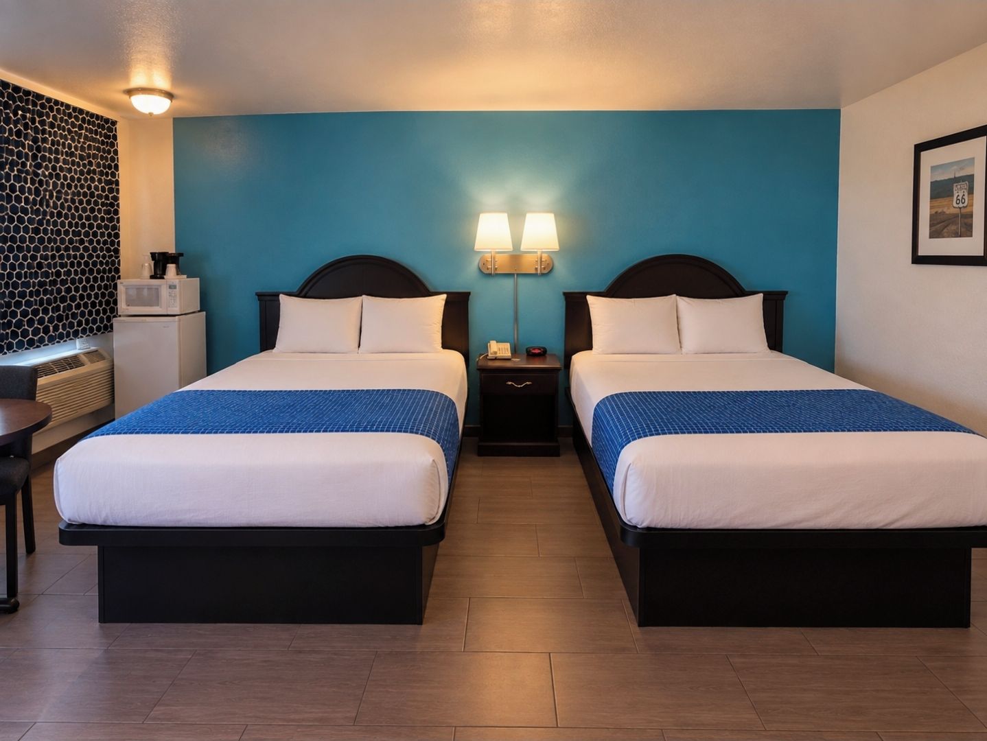A hotel room with two beds, a desk, a microwave, and a wall-mounted heater.
