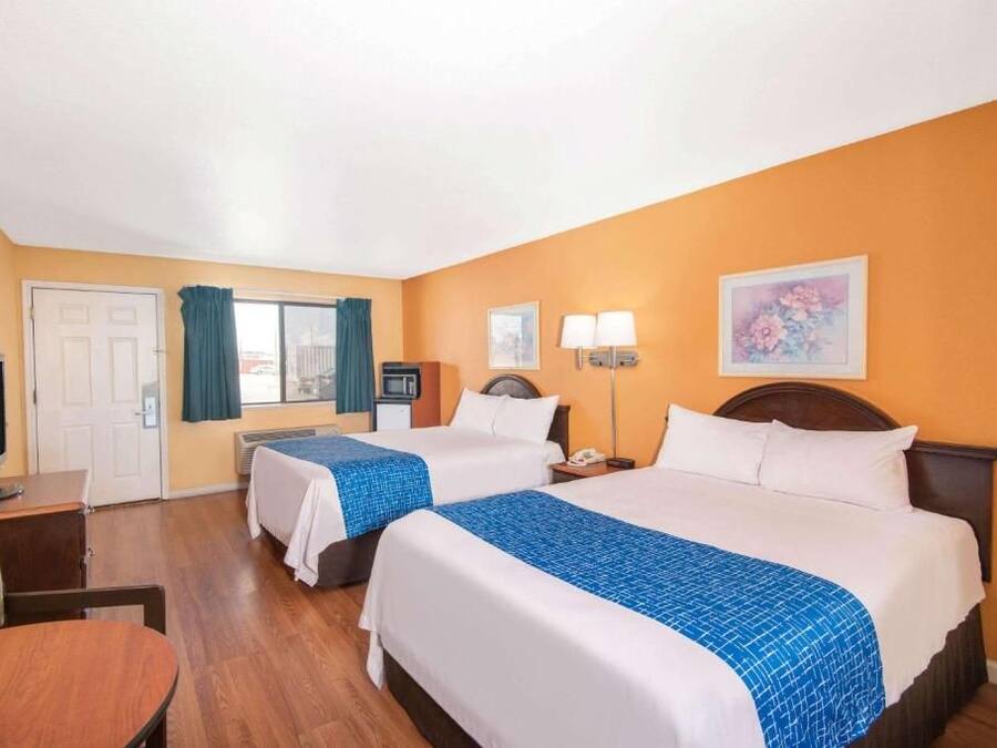 A hotel room with two beds, a desk, a television, and a window with curtains.