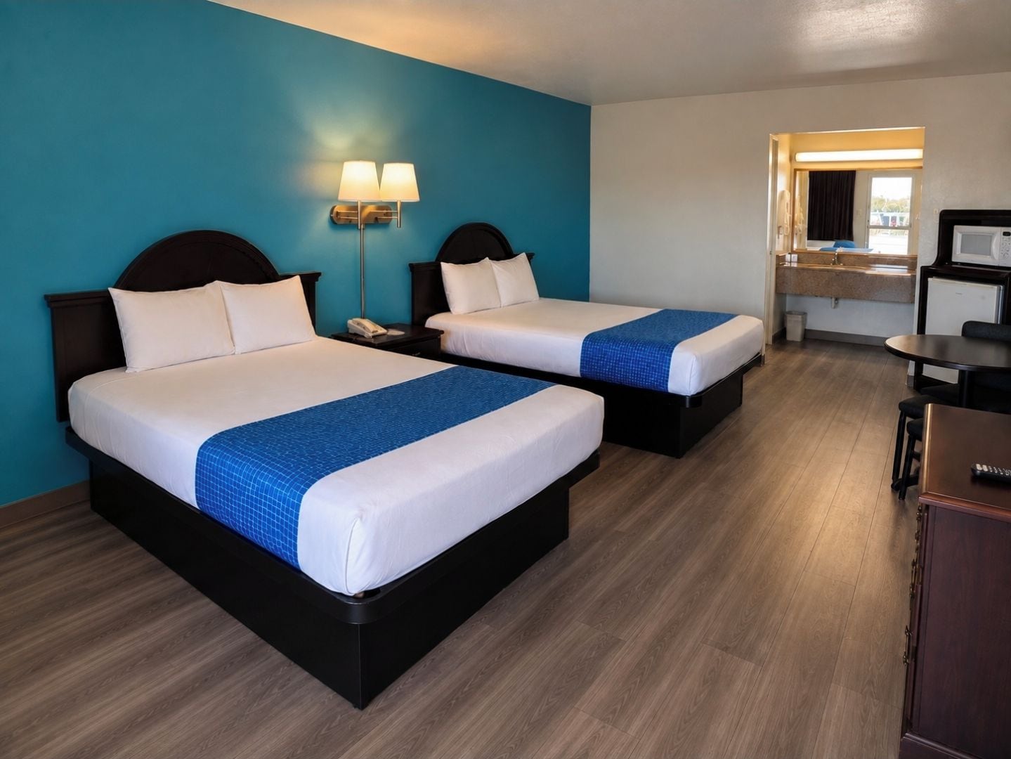 A hotel room with two beds, a desk, a chair, a microwave, and a window with curtains.