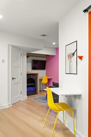 Ein modernes Interieur mit einer weißen Tür, einem gelben Stuhl, einem weißen Schreibtisch und einem farbenfrohen abstrakten Gemälde.