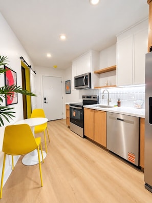 A modern kitchen with white cabinets, stainless steel appliances, and a yellow dining table with matching chairs. - Trendy 1BR | Montrose | Sleeps 4 (Houston)