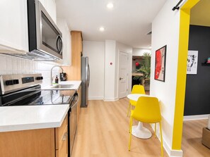 A modern kitchen with stainless steel appliances, a white countertop, and a dining area with yellow chairs. - Trendy 1BR | Montrose | Sleeps 4 (Houston)