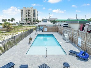 A rectangular pool with a diving board, surrounded by a wooden fence, and a beach in the background. - Yacht Harbor House (Pensacola)