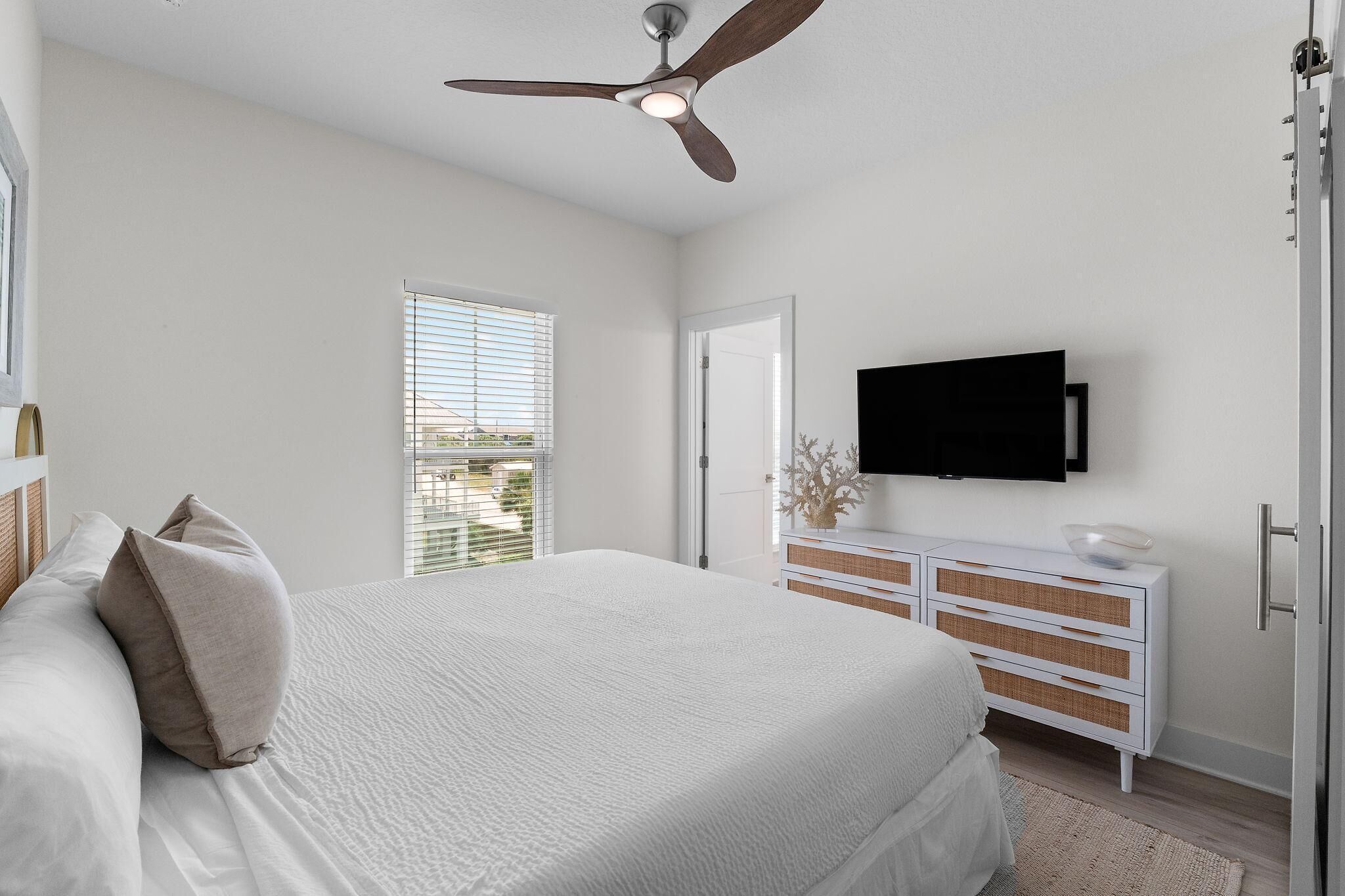 A bedroom with a bed, a dresser, a television, and a ceiling fan.