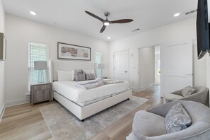 A bedroom with a bed, bedside tables, a ceiling fan, and a door leading to another room. - Yacht Harbor House (Pensacola)