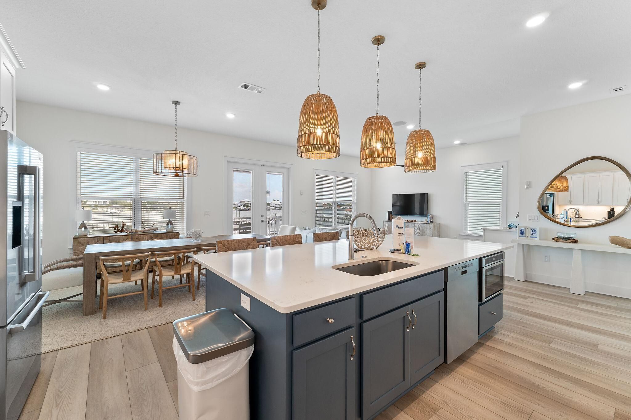 A modern kitchen with a large island, pendant lights, and a view to the outside.