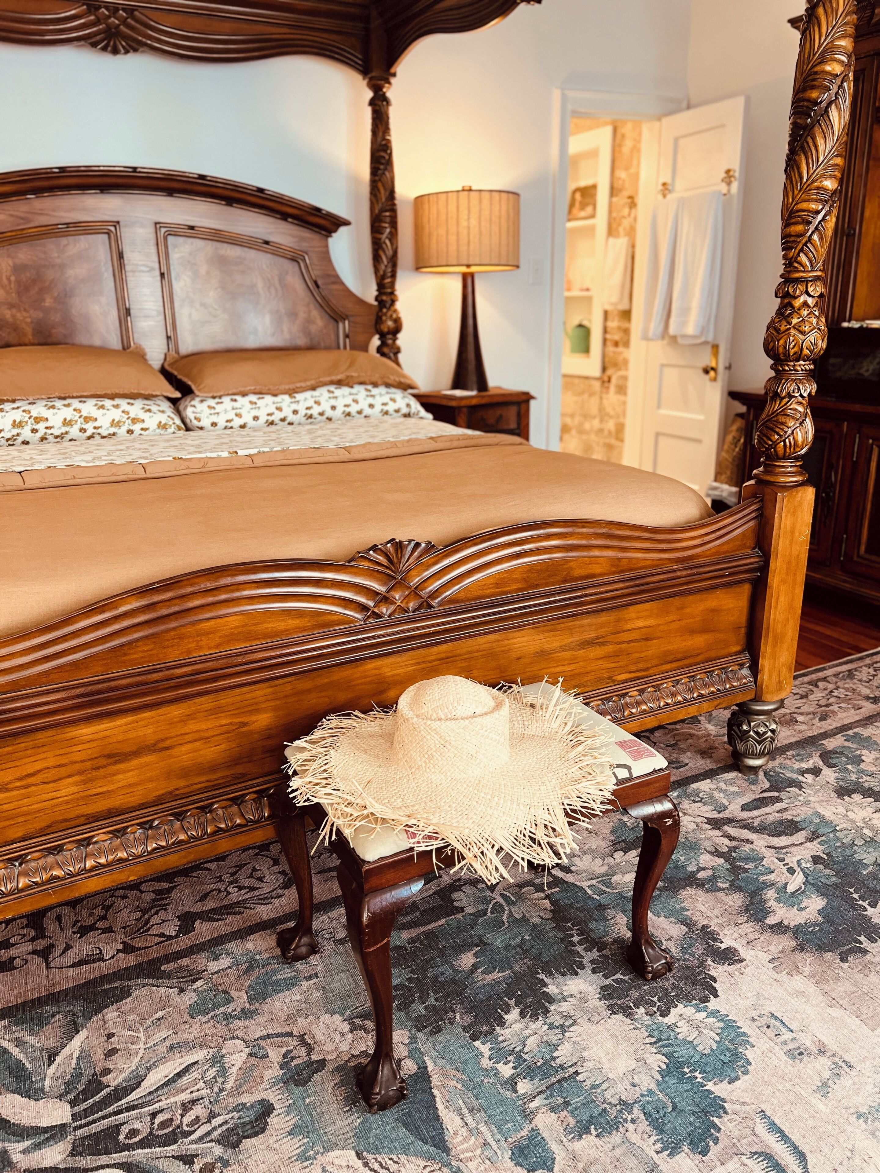 A bedroom with a four-poster bed, a bedside lamp, and a woven basket on a matching chair.