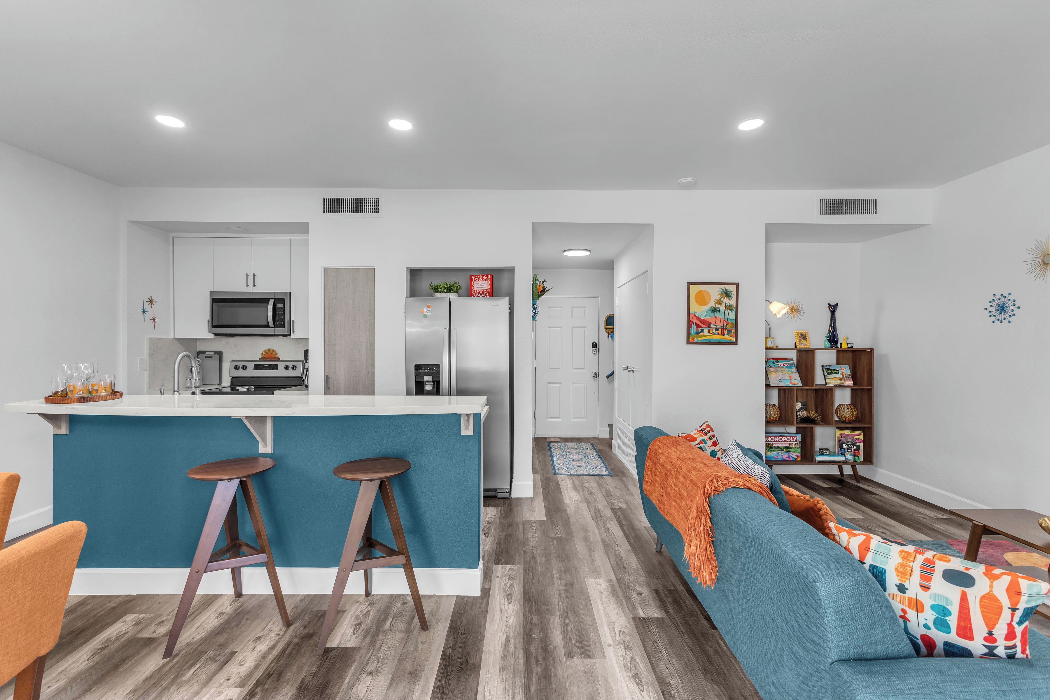 A modern kitchen with a central island, bar stools, and a dining area with a sofa and coffee table.