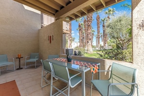 An outdoor patio with a table and chairs, a view of palm trees, and a textured wall. - Indian Wells Condo, Steps to Pool,  Minutes to La Quinta El Paseo and Coachella (Indian Wells)