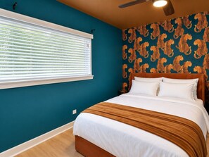 A bedroom with a bed, a window with blinds, a ceiling fan, and a patterned wallpaper. - 1BR + Sofa Bed | Trendy Montrose (Houston)