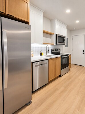 A modern kitchen with stainless steel appliances, wooden cabinets, and a white countertop. - 1BR + Sofa Bed | Trendy Montrose (Houston)