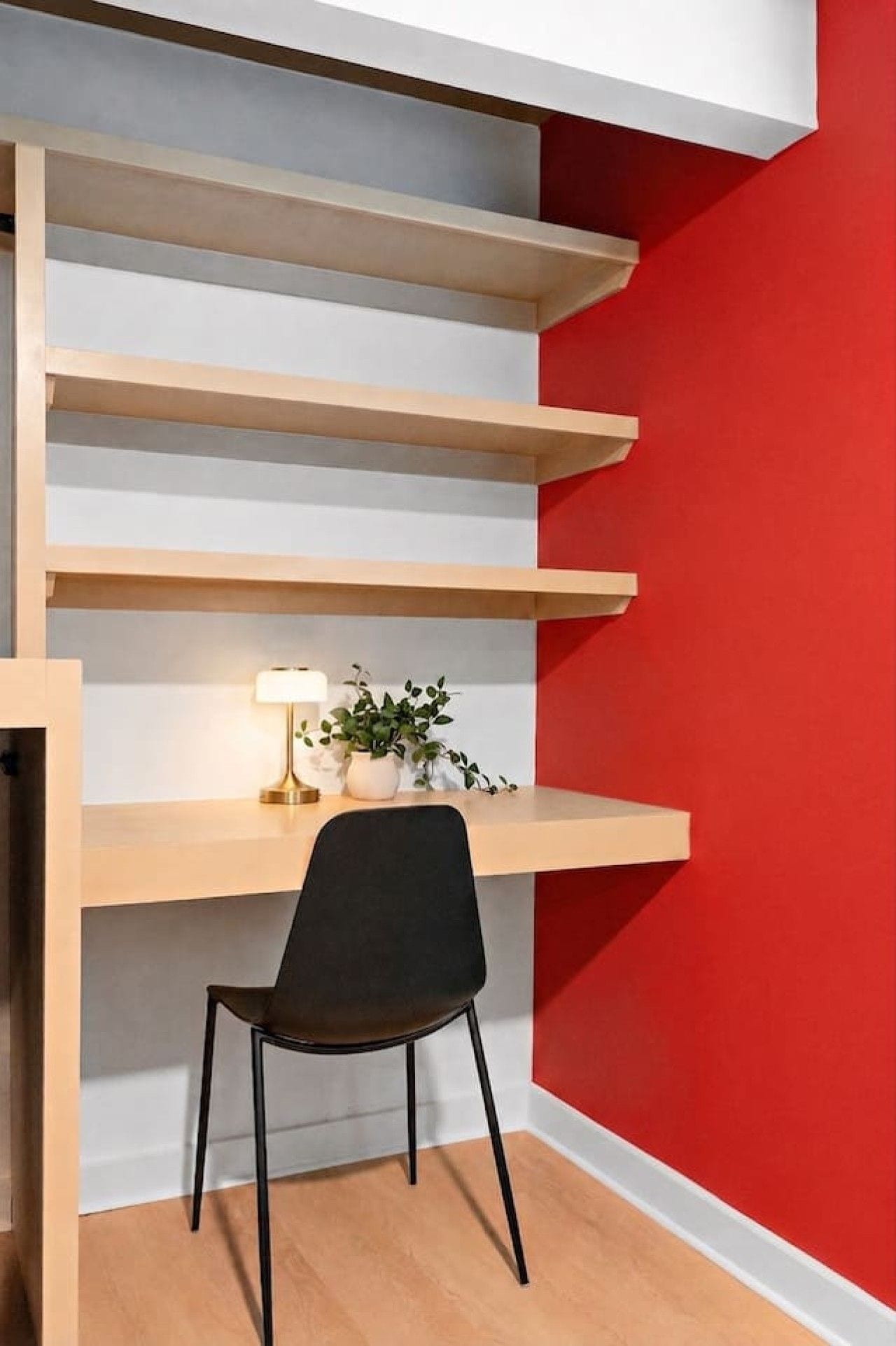 Un espacio de trabajo moderno con escritorio, silla y estantería frente a una pared roja.