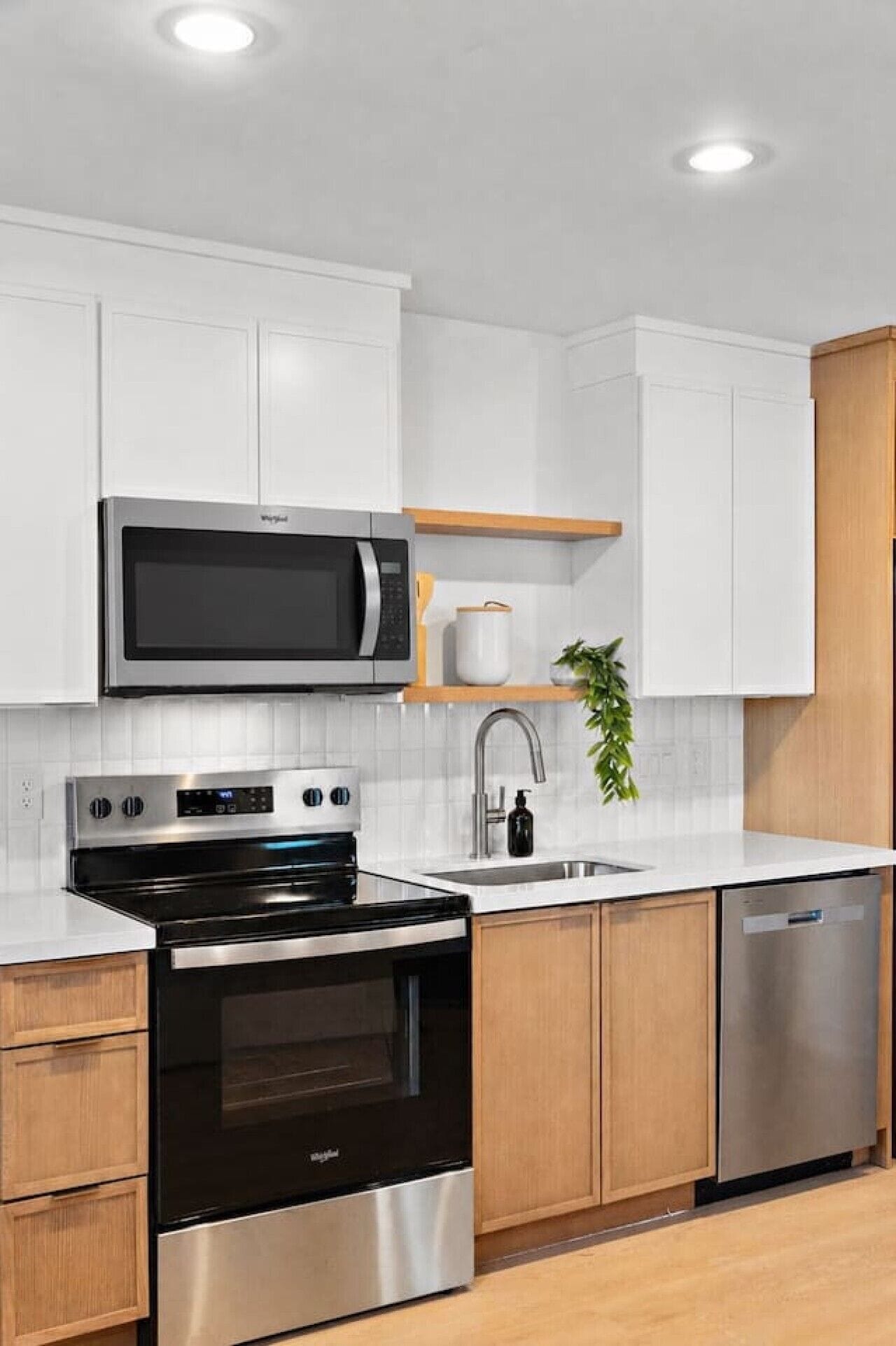 A modern kitchen with white cabinetry, a stainless steel microwave, oven, and dishwasher, and a wooden countertop.