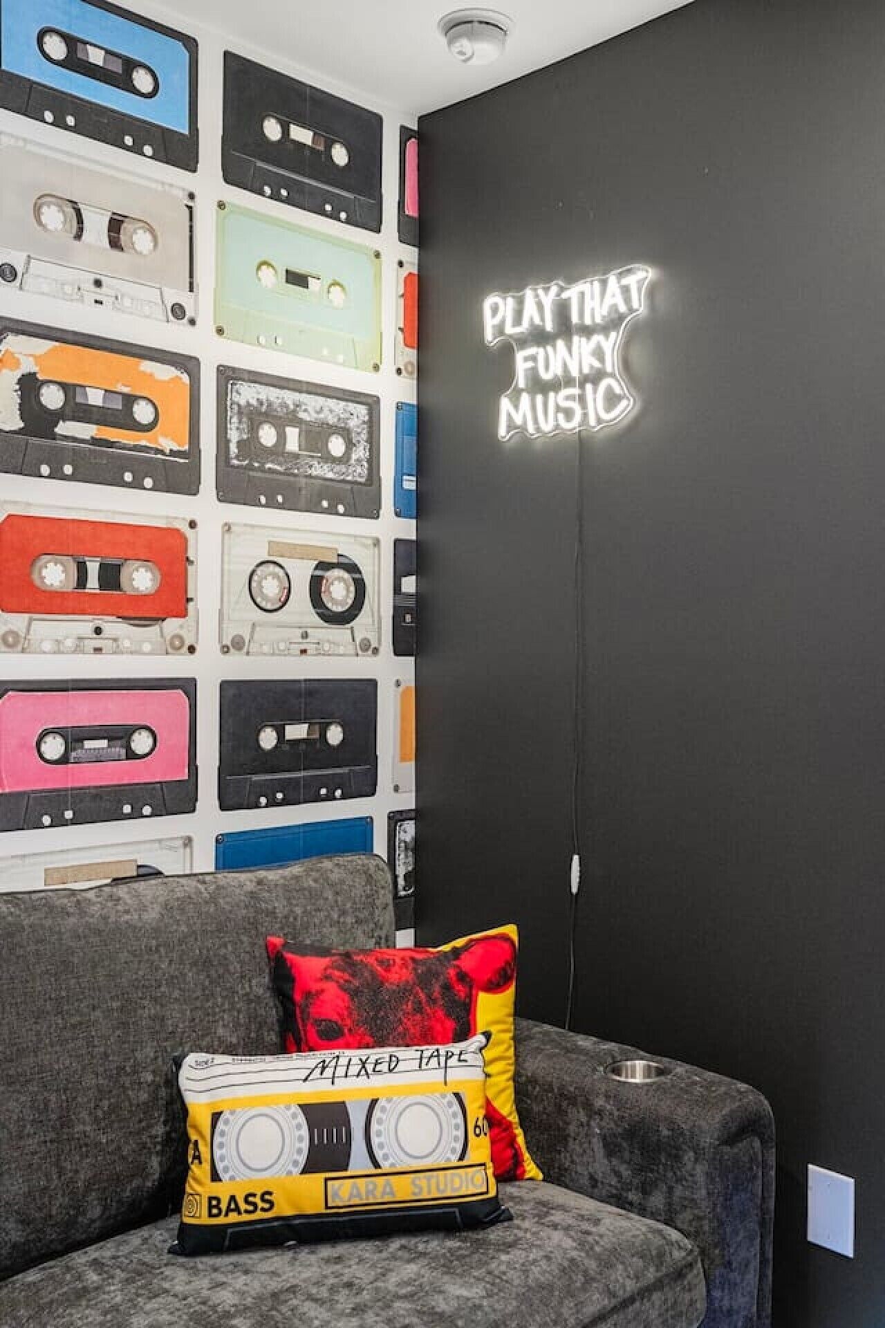 Ein Zimmer, dessen Wand mit verschiedenen Kassetten und einem Neonlichtschild, auf dem 'PLAY THAT FUNKY MUSIC' steht, dekoriert ist.