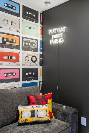 A room with a wall decorated with various cassette tapes and a neon sign that reads 'PLAY THAT FUNKY MUSIC'. - Designer 1BR | Sleeps 4 | Free Parking (Houston)