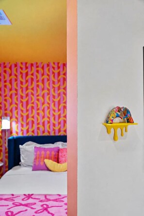 Ein Zimmer mit einem Wandteppich, einem Bett mit Kissen und einem an der Wand befestigten Regal mit einem farbenfrohen Gegenstand.
