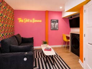 Ein Wohnzimmer mit einer Couch, einem Couchtisch, einer Pflanze und einem Neon-Schild an der Wand.