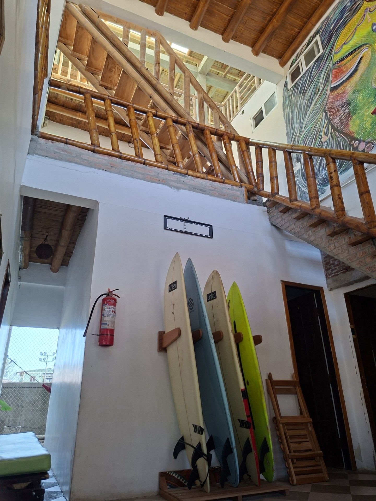 Un bâtiment à plusieurs niveaux avec un escalier en bois, un extincteur et des planches de surf appuyées contre le mur.
