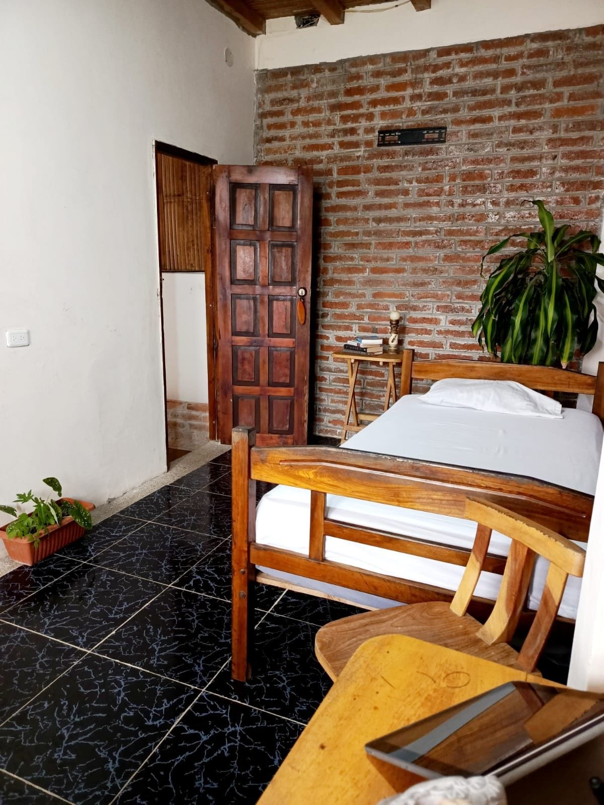 Una habitación con una cama, un escritorio de madera, una planta en maceta y una pared de ladrillo.