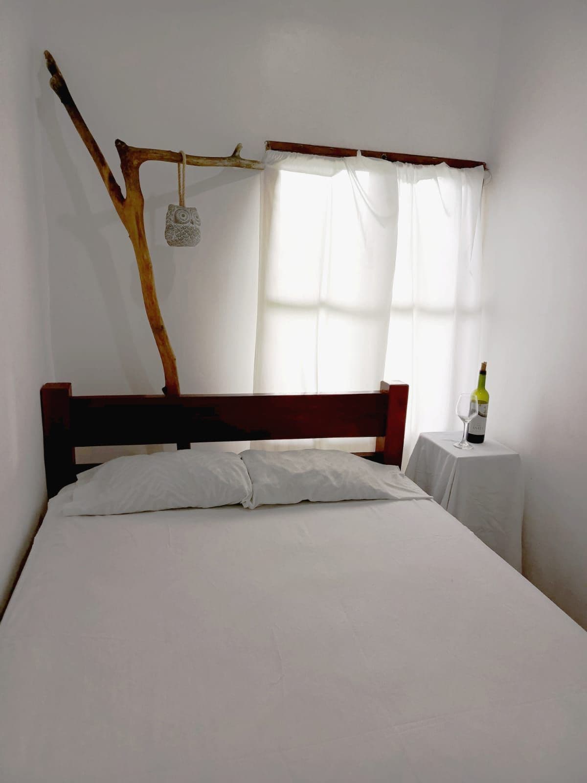 Una cama con ropa blanca, un cabecero de madera y una mesita de noche con una botella de vino.